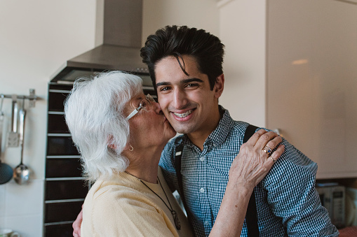 Teenage boy is smiling for the camera while his grandmother kisses his cheek.