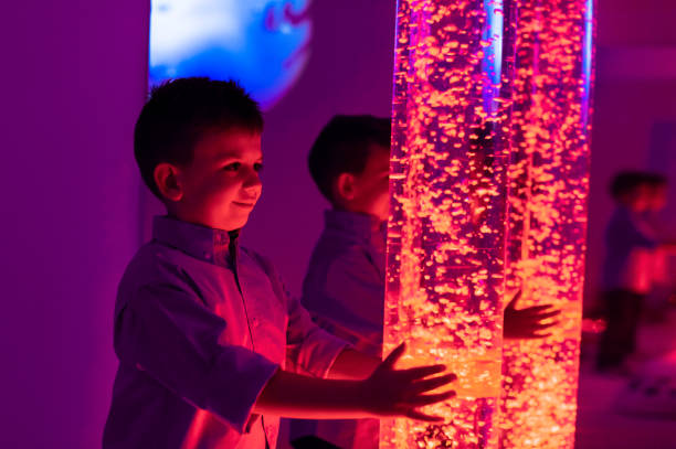 istock Child in therapy sensory stimulating room, snoezelen. Child interacting with colored lights bubble tube lamp during therapy session. 1130452039