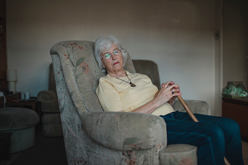 Senior woman is asleep in an armchair in the living room of her home.