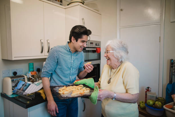 Taste Testing Lunch at Grandma's Teenage boy and his grandmother are laughing in the kitchen together after the teenager has taken a potato chip from the tray his grandmother has removed from the oven. family eating potato chips stock pictures, royalty-free photos & images