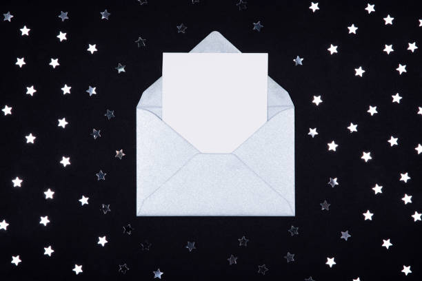 istock White blank card in opened silver grey envelope on black background decorated with star confetti. 1130459788