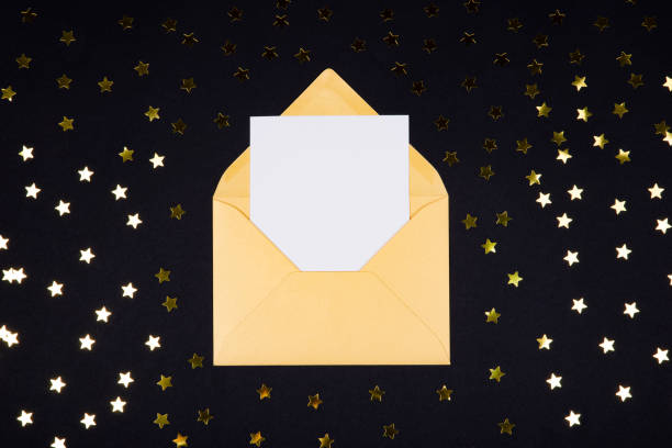 istock White blank card in opened golden color envelope on black background decorated with star confetti. 1130459796