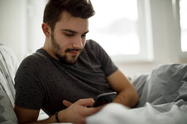 istock Attractive young man using mobile phone in the bed 1130459922
