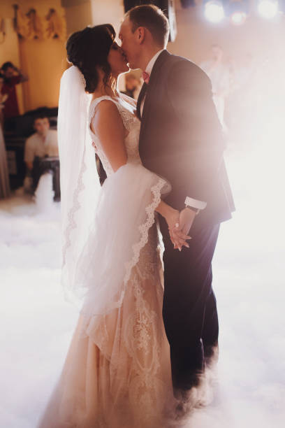 istock Gorgeous bride and stylish groom performing first dance in light at wedding reception in restaurant. Luxury wedding couple sensually dancing and embracing, romantic moment 1130460954