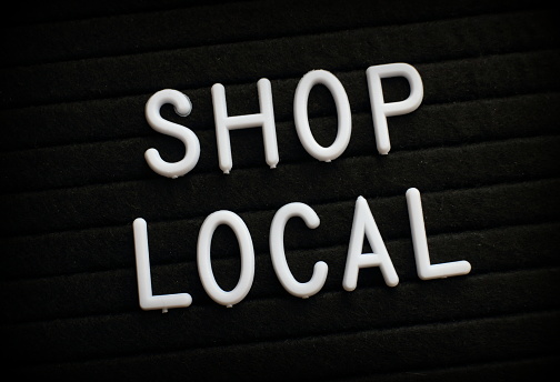 The words Shop Local in white plastic letters on a black bulletin board as a reminder