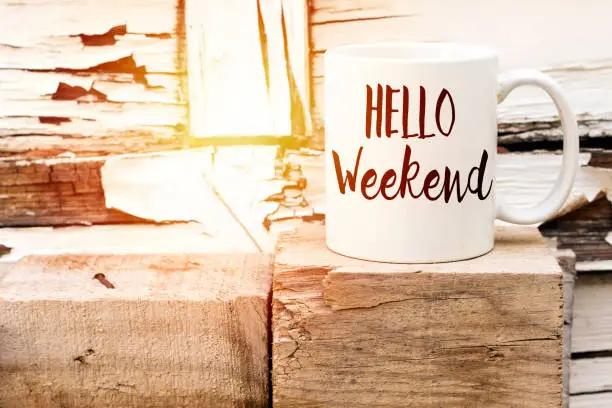 Photo of text HELLO weekend on cup of aromatic coffee on wooden cube