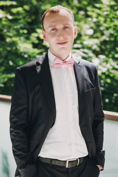 세련 된 행복 한 신랑 포즈 핑크 나비 넥타이 검은색 양복 야외, 결혼식 하기 전에 아침에 준비 하 고. 풍부한 실업가 웃 고 - necktie pink shirt luxury 뉴스 사진 이미지
