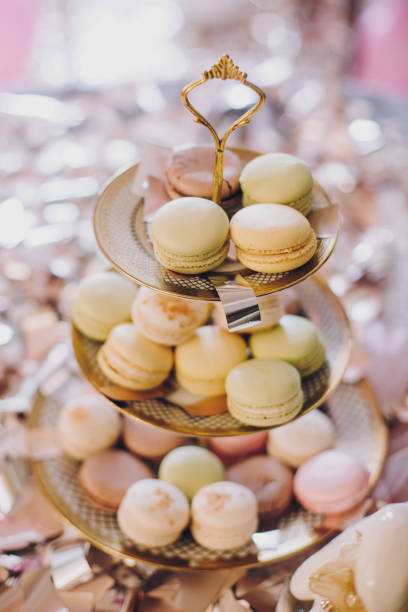 Delicious colorful macarons on beautiful vintage stand with gold ornaments on table with gold and silver confetti. Luxury catering. Bridal hen or baby shower. French dessert macaroons