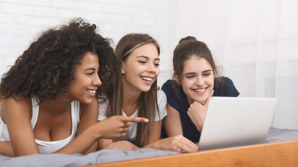 Relaxed female friends using laptop in bed Relaxed female friends using laptop, watching photos in bed at home divergent movie review stock pictures, royalty-free photos & images