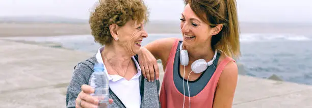 Senior sportswoman laughing with female friend by sea pier