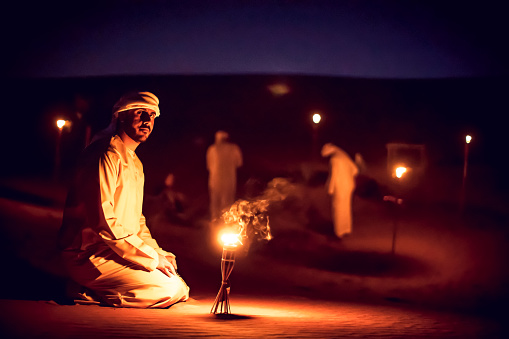 Árabe media sentada en las dunas de arena cerca de una lámpara de aceite en un camping photo
