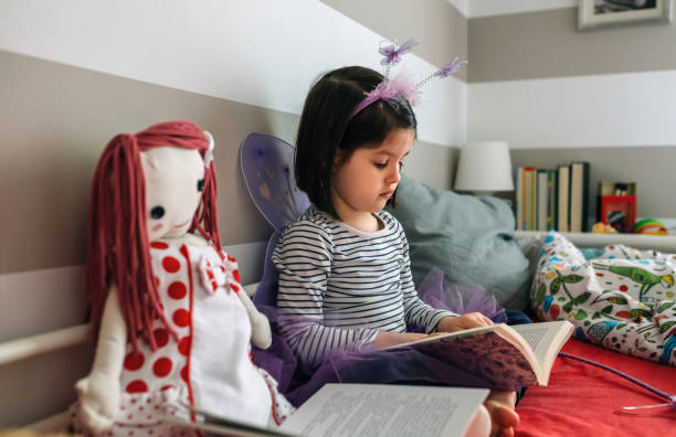istock Girl disguised as a butterfly reading with her doll 1130467544