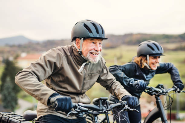 couple de personnes âgées actives avec electrobikes vélo à l’extérieur sur une route dans la nature. - cycling senior adult sports helmet men photos et images de collection