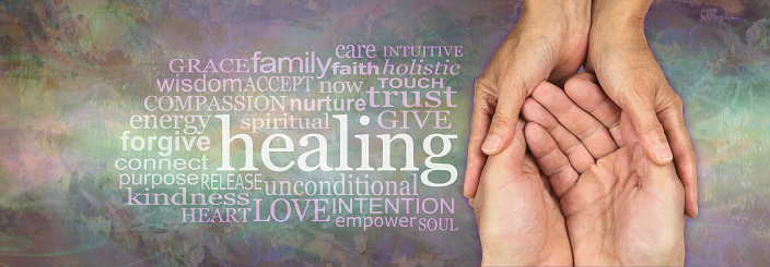 Female hands gently cupped around male open hands on a rustic muted multicoloured stone effect background with a HEALING word cloud