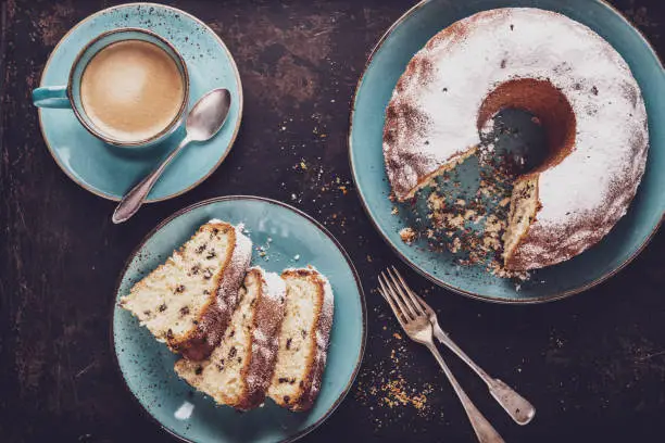 Photo of freshly baked gugelhupf with a cup of coffee crema on a dark background, top view