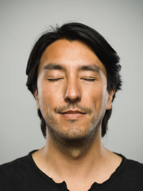 Portrait of real hispanic man with blank expression and eyes closed Close up portrait of adult hispanic man with blank expression and eyes closed against white gray background. Vertical shot of colombian real people resting in studio with black hair and dark eyes. Photography from a DSLR camera. Sharp focus on eyes. blank expression photos stock pictures, royalty-free photos & images