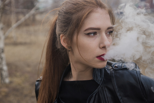 The girl lets out steam from the mouth. Redhead vape girl.