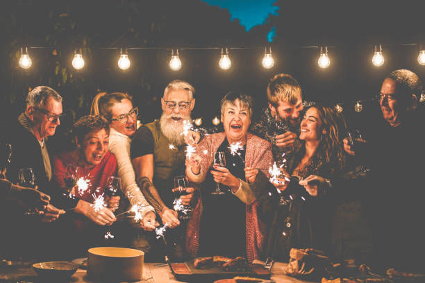 happy family and friends celebrating with sparkler fireworks after dinner - different age of people having fun drinking wine at birthday bbq party outdoor - celebration concept - focus on center faces - tattoo father family son imagens e fotografias de stock