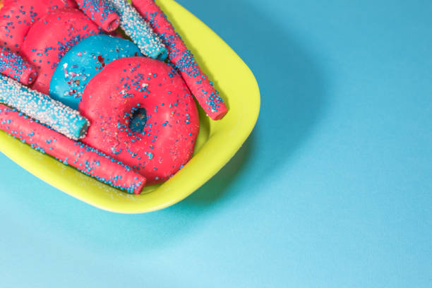 Glazed donuts with sprinkles and candy sticks on color background