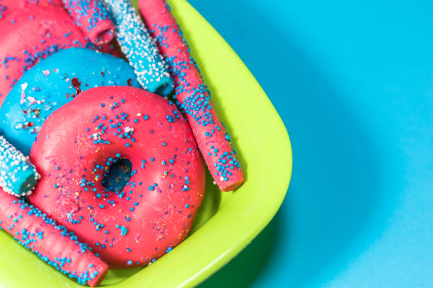 Glazed donuts with sprinkles and candy sticks on color background