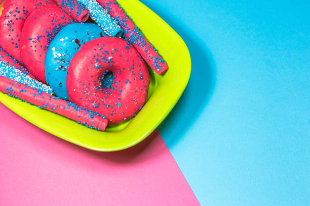 Glazed donuts with sprinkles and candy sticks on colorful background