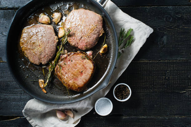 istock Roast Beef steak in a frying pan, cooking. Top view, black background. 1130488914