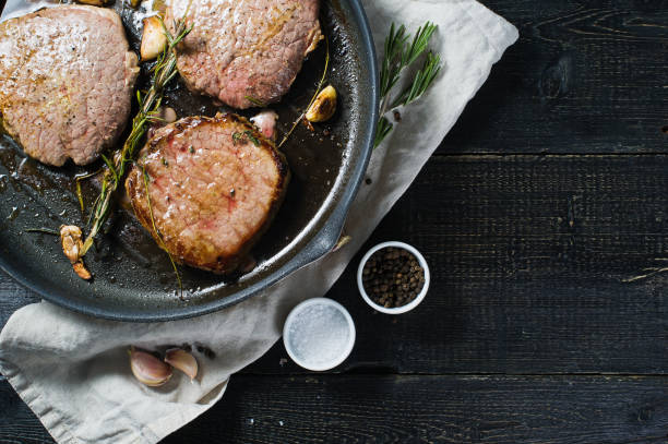 istock Roast Beef steak in a frying pan, cooking. Top view, black background. 1130488918