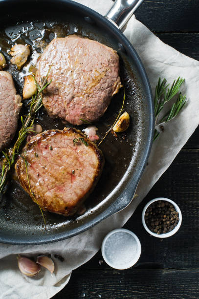 istock Roast Beef steak in a frying pan, cooking. Top view, black background. 1130488925