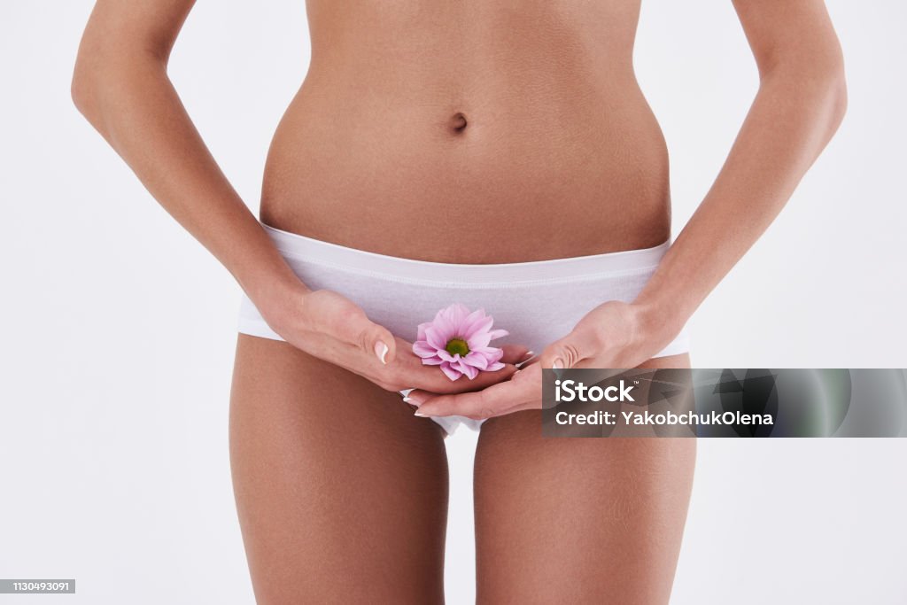 Young lady holding beautiful pink flower near underwear Beauty and health. Close up of well-shaped woman in white panties covering intimate area with flower Panties Stock Photo