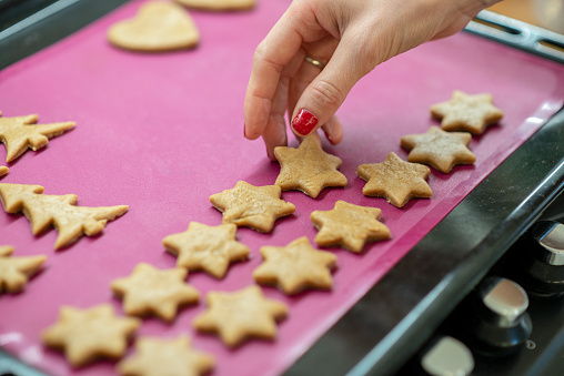Female hand placing star shaped cookie dough on a pink baking mat.