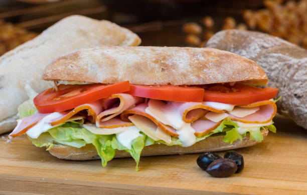 istock Rustic flour topped ciabatta bread rolls filled with salad & cut meat rotating on wooden surface. 1130506801