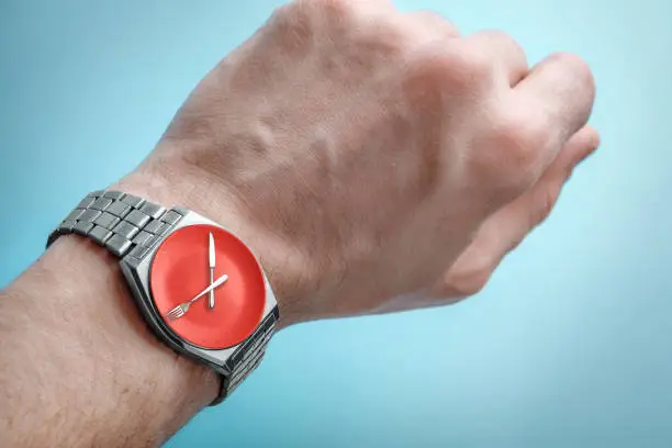 Wrist watch on man's hand. Plate, knife and fork on clock face. Concept of intermittent fasting, lunchtime