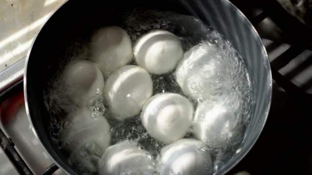 A lot of white eggs lie and boil in a metal pan in boiling water. Close up. The view from the top. 4K.