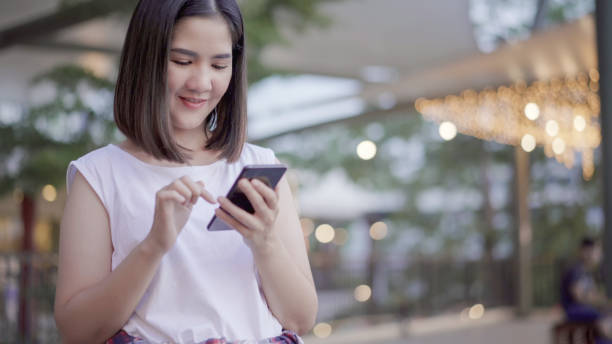 istock Asian woman using smartphone while standing at shopping mall 1130514599