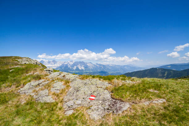 Hiking mark sign red white red painted on rock on mountain Reiteralm with distant view to mountain Dachstein in Austria