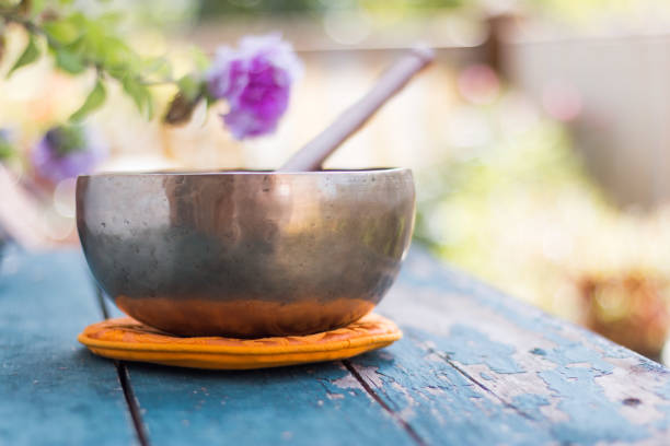 Singing bowl on a rustic wooden table with flowers, zen, outdoors stock photo