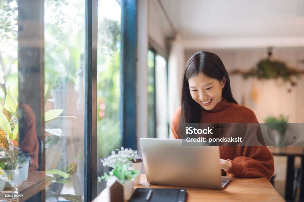 Asian woman working at a coffee shop with a laptop Happy young Asian girl working at a coffee shop with a laptop. Laptop Stock Photo