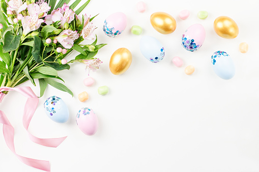 Festive Easter background with decorated eggs, flowers, candy and ribbons in pastel colors on white background