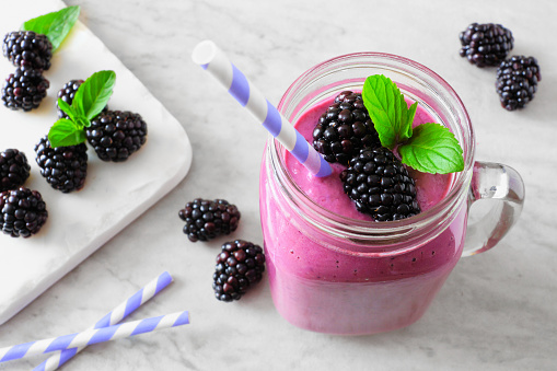 Healthy blackberry smoothie in a mason jar glass. Close up, downward view table scene against a white marble background.