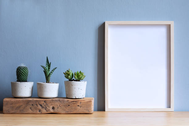 Minimalistic room interior with mock up photo frame on the brown wooden table with beautiful cacti in design hipster cement pot. Grey walls. Stylish and floral concept of mock up poster frame. Minimalistic home interior with composition of home garden. Plants love. surrounding wall photos stock pictures, royalty-free photos & images