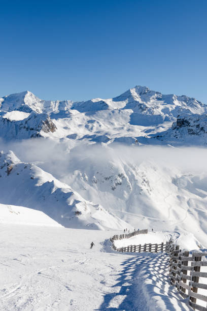 Unidentified skiers skiing on a ski slope in pristine alpine landscape. Calm and tranquil winter scenery in French Savoy Alps, ski resort La Plagne Unidentified skiers skiing on a ski slope in pristine alpine landscape. Calm and tranquil winter scenery in French Savoy Alps, ski resort La Plagne la plagne photos stock pictures, royalty-free photos & images