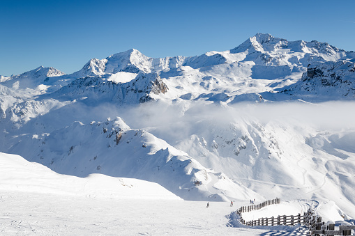 Unidentified skiers skiing on a ski slope in pristine alpine landscape. Calm and tranquil winter scenery in French Savoy Alps, ski resort La Plagne