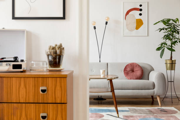 istock Retro interior of living room with design commode, coffee table vinyl recorder, cacti and mock up posters frames on the white walls. Cozy room with brown wooden parquet and plants. 1130535637