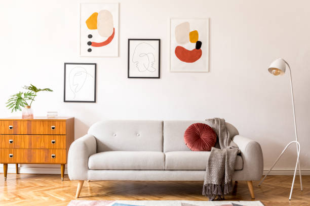 istock Stylish vintage decor in a spacious flat interior with design grey sofa, armchair, retro commode and posters on the wall. Brwon wooden parquet, stylish carpet and plants. Bright living room. 1130536117