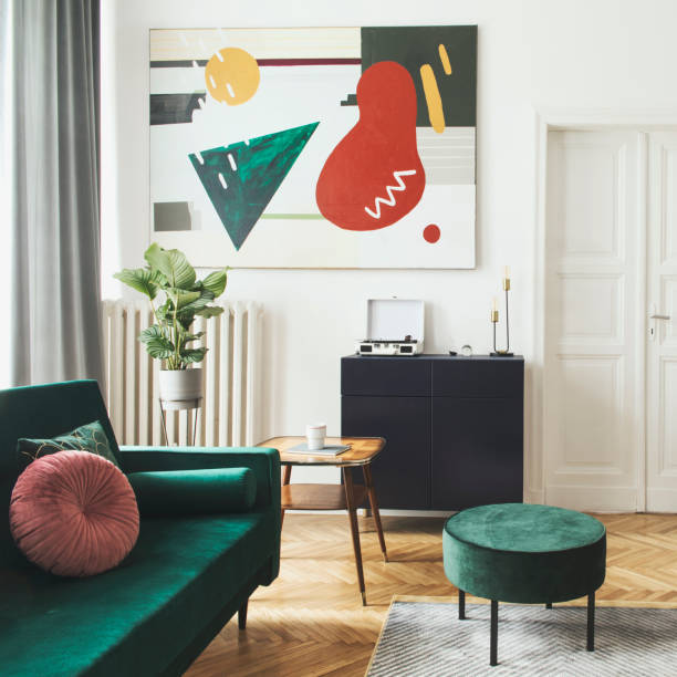 istock Luxury home interior with design velvet sofa, coffee table, pouf, commode and accessroies. White walls with painting. Sunny view. Stylish decor of sitting room. 1130537091