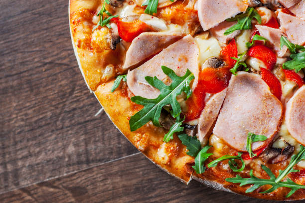 istock Pizza with Mozzarella cheese, mushrooms, ham, tomato sauce, pepper, Spices and Fresh arugula. Italian pizza on wooden table background 1130540566