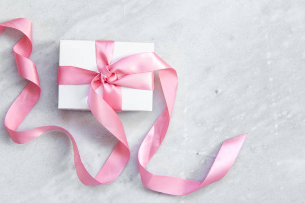 Tied, fluffy decor bow with white ribbon adorned with red dots for gift box wrapping. Wrapping paper ribbon with bow isolated on white background. Elegant paper ribbon with bow, for gift packaging.