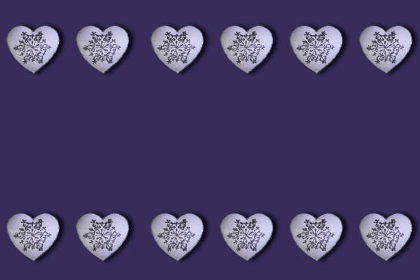White hearts with glitter silver snowfalakes pattern on a purple background. Saint Valentine's Day concept. Flat lay. Top view.