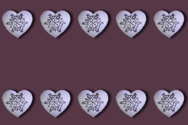 White hearts with glitter silver snowfalakes pattern on a burgundy background. Saint Valentine's Day concept. Flat lay. Top view.