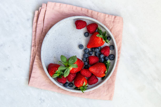 istock Mixed berries in conrete plate on marble background with empty plate and copy space 1130544719